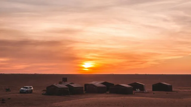 Hilera de jaimas de un campamento del desierto bajo un cielo naranja al atardecer