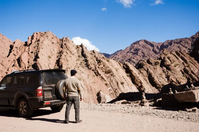 4x4 parked on a mountain piste below folded red rock ridges