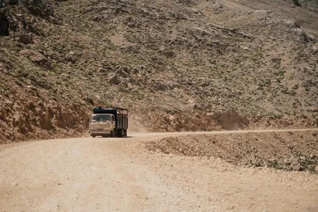 Truck on a dusty dirt road along a rocky mountain slope