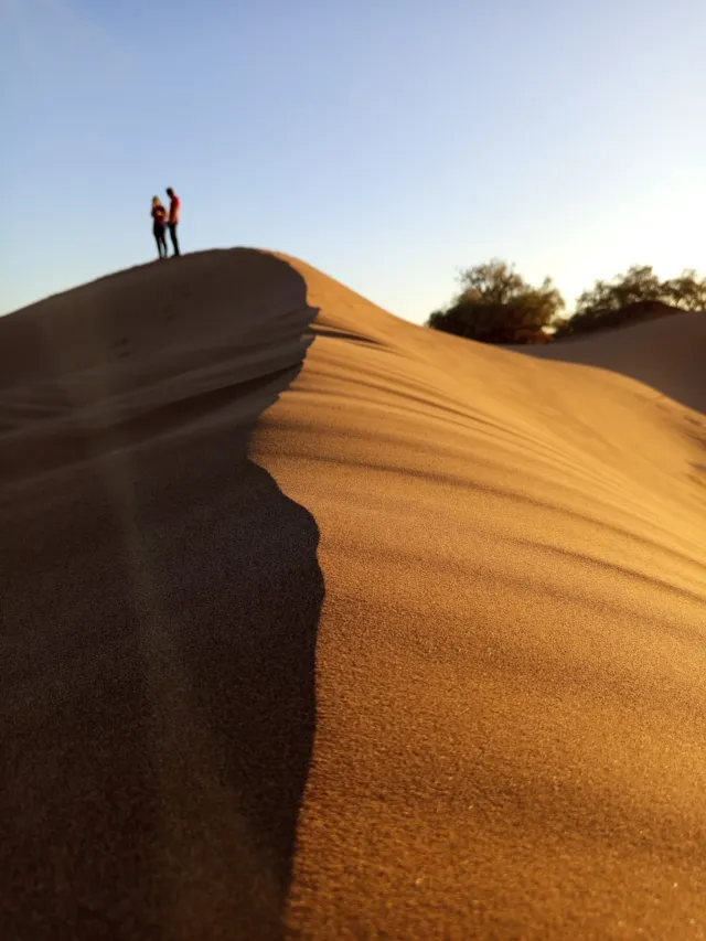 Two small figures on the sharp crest of a tall dune