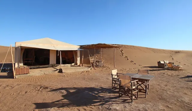 Large white camp tent with a shaded terrace on the sand