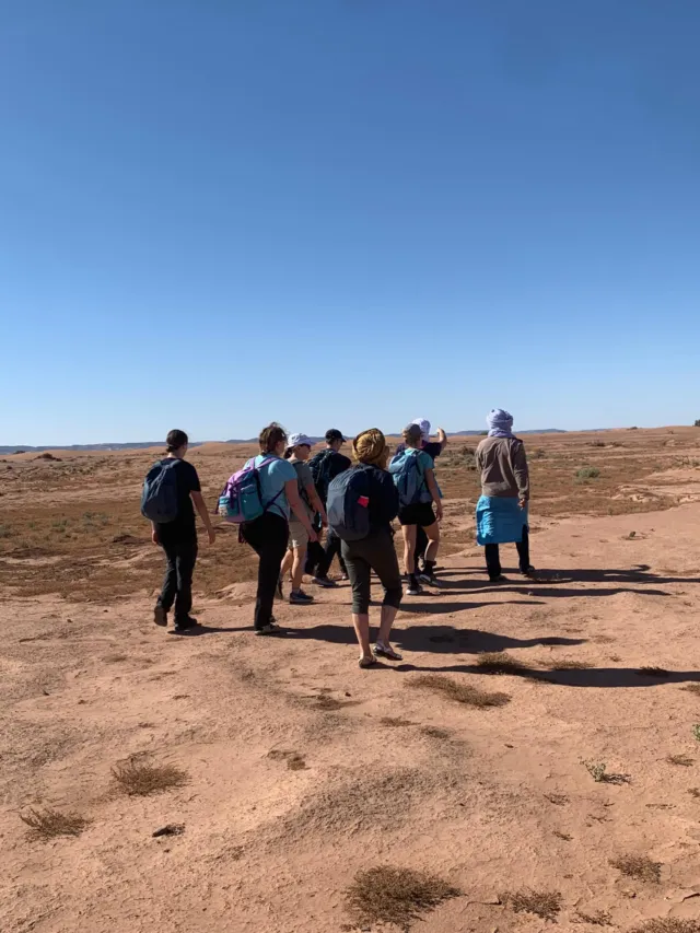 Groupe de marcheurs avec sacs à dos traversant une plaine désertique caillouteuse